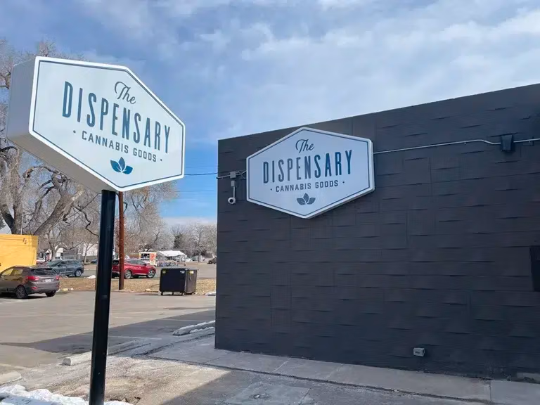 The black exterior of The Dispensary littleton, with it's light up The Dispensary Cannabis Goods sign